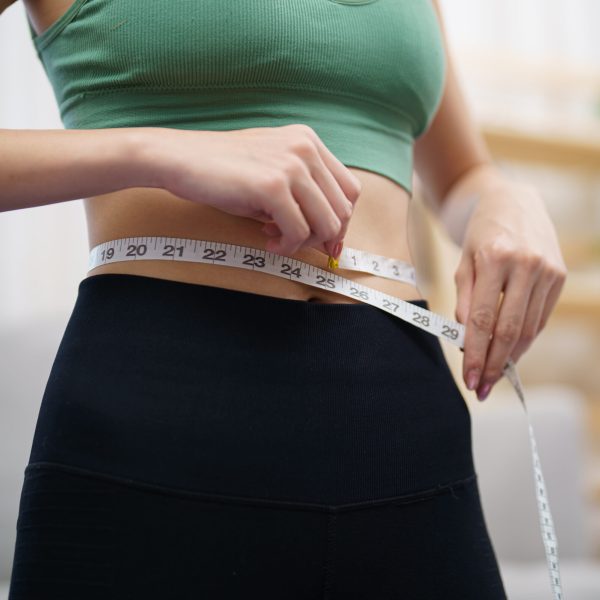 Asian healthy woman dieting Weight loss. Slim woman measuring waist with measure tape after diet at home weight control