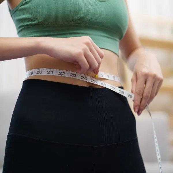Asian healthy woman dieting Weight loss. Slim woman measuring waist with measure tape after diet at home weight control